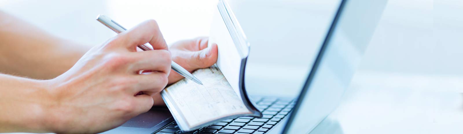 Person writing a check in front of a laptop.