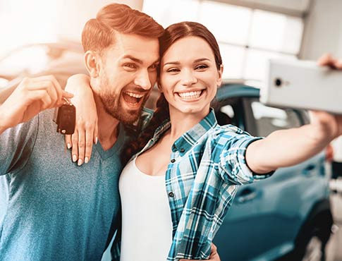 Couple taking a selfie in from of their new car.