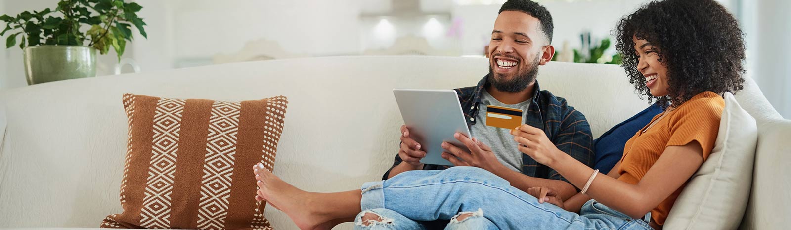 Young couple sitting on couch using a tablet and making an online purchase.